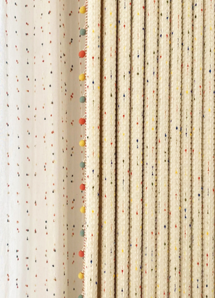 a close-up view of a beige curtain with a pattern of multicolored dots, creating a vibrant and lively visual effect.