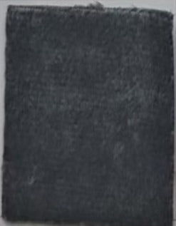 A square-shaped object with a dark gray or black color, possibly made of a material like fabric or paper.