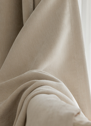 A close-up view of a beige fabric, possibly a curtain or fabric, with a soft, flowing texture.