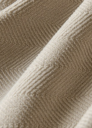A close-up view of a textured fabric, possibly a piece of clothing or a textile, with a subtle pattern and a soft, beige color.