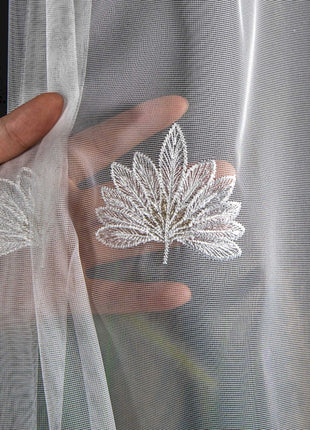 a person's hand holding onto a sheer curtain with a leaf embroidered on it