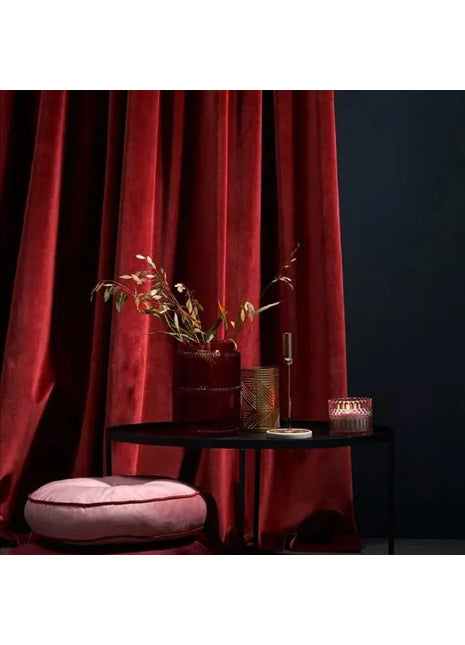 a black table with a pink cushion and a red curtain