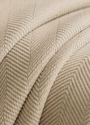 a close-up view of a textured fabric, possibly a blanket or a piece of clothing, with a herringbone pattern. The fabric appears to be a light beige color, and the texture is visible, suggesting it is soft and comfortable.