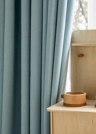 a child's room with blue curtains and a wooden dresser