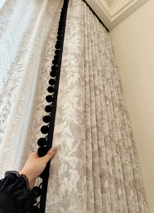 A hand is holding a curtain rod with decorative black balls, which is attached to a set of curtains with a floral pattern.