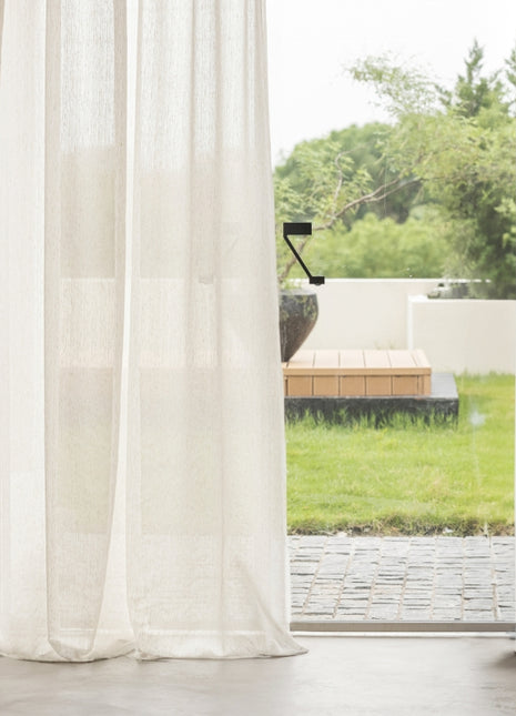 a window with a white curtain and a wooden bench
