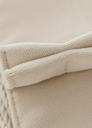 A close-up view of a beige fabric, possibly a blanket or cushion, with a slightly wrinkled texture.