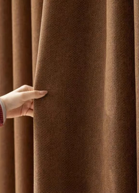 A hand is holding a brown curtain, examining its texture and color.
