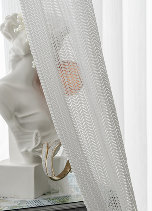 a white bust of a person, partially obscured by a white curtain with a zigzag pattern.