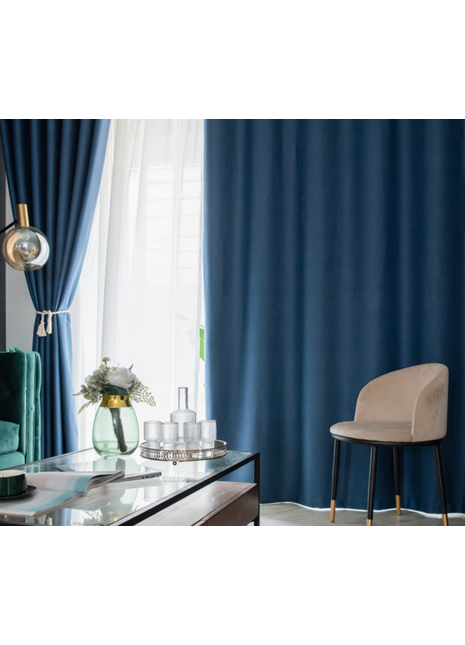 a living room with a blue curtain, a glass coffee table with a vase of flowers and a tray of glasses, a beige armchair, and a white lamp.