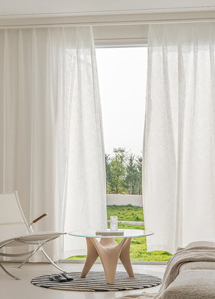 a living room with a glass table and white curtains