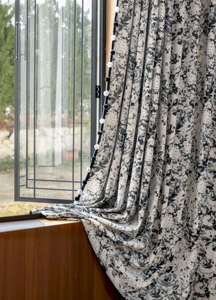 a window with a black and white flowered curtain