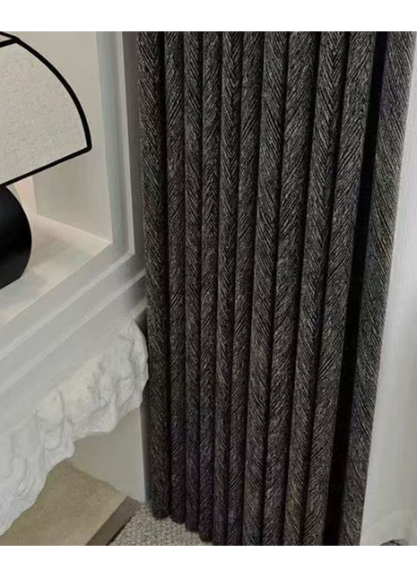 a close-up view of a dark grey curtain with a herringbone pattern, hanging next to a white wall.