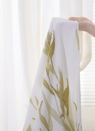 a person is holding a white curtain with gold leaves