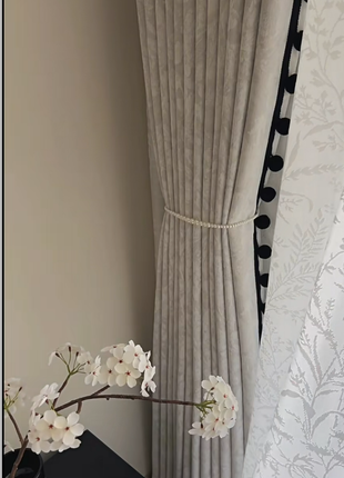 a white curtain with a floral pattern, a vase with white flowers, and a black table.