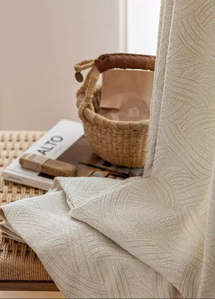 Tissu du rideau blanc cassé moderne posé près d'un panier en osier et de livres