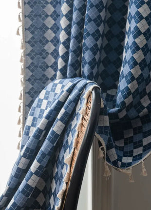 Rideau bicolore à damier bleu et écru, bas à pompons, drapé sur une chaise noire